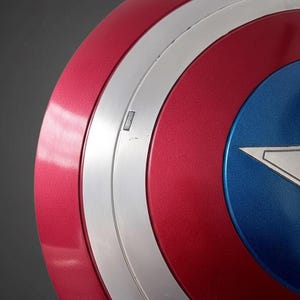 May include: A close-up of a red, white, and blue shield with a metallic finish. The shield has a circular design with a silver band and a blue star in the center. The text "MEDIEVAL ARMORY CO" is visible.