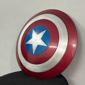 May include: A circular shield featuring a concentric design with a deep red outer ring, a brushed silver middle ring, and a vibrant blue center circle. A prominent five-pointed silver star is centered within the blue circle, creating a bold look.