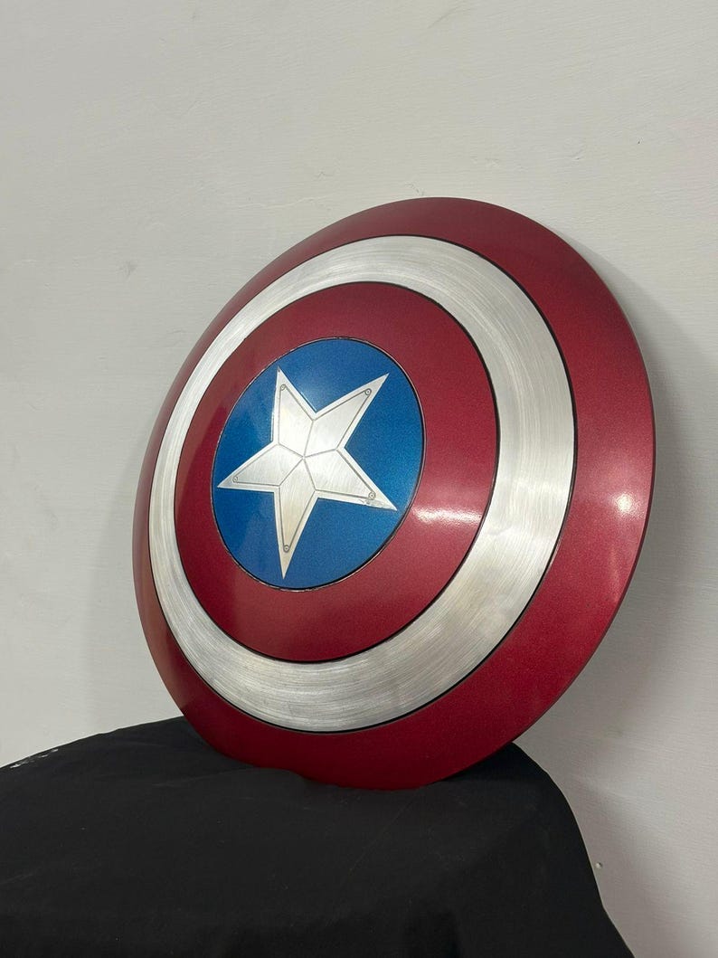May include: A circular shield featuring a concentric design with a deep red outer ring, a brushed silver middle ring, and a vibrant blue center circle. A prominent five-pointed silver star is centered within the blue circle, creating a bold look.