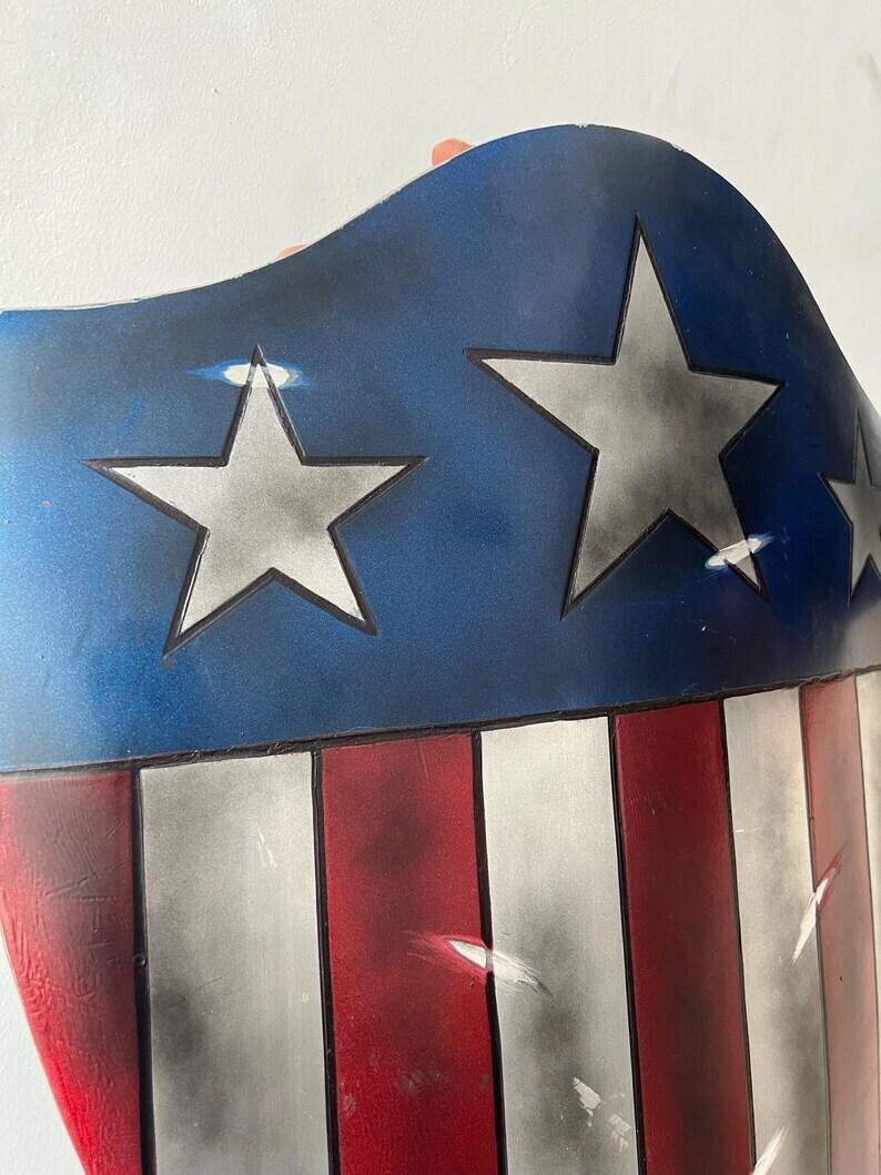 Op de afbeelding: Een schild met een blauw bovenstuk met zilveren sterren en een rood-wit gestreept onderstuk. Het ontwerp is ge&iuml;nspireerd op de Amerikaanse vlag, met een gebogen bovenrand.