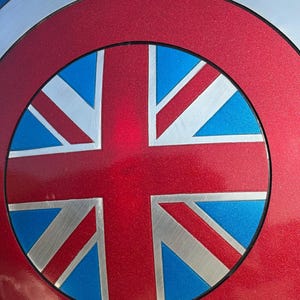 Op de afbeelding: Een metalen schild met een rood, wit en blauw ontwerp. Het midden toont een rode cirkel met een Union Jack vlagontwerp in zilver, blauw en rood. De buitenste ring is zilver, wat een patriottisch, superheldenachtig effect cre&euml;ert.