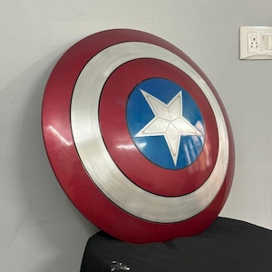 May include: A circular shield featuring a concentric design with a deep red outer ring, a brushed silver middle ring, and a vibrant blue center circle. A large, five-pointed silver star is centered within the blue circle, creating a bold, metallic appearance.