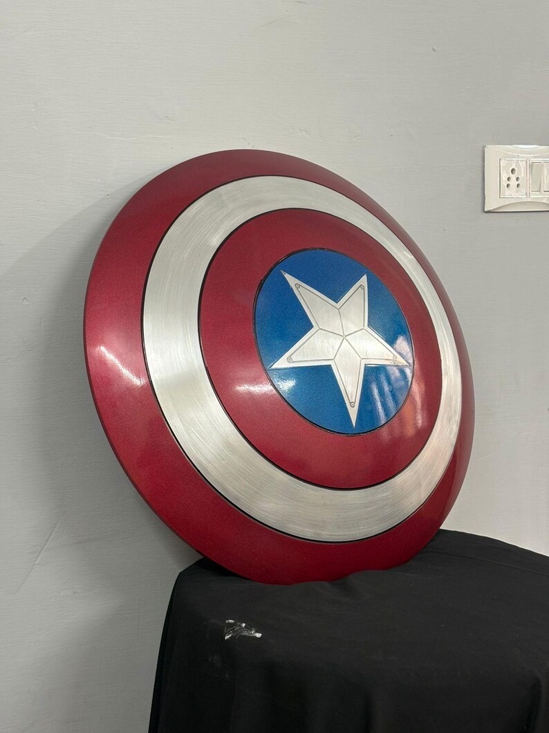 May include: A circular shield featuring a concentric design with a deep red outer ring, a brushed silver middle ring, and a vibrant blue center circle. A large, five-pointed silver star is centered within the blue circle, creating a bold, metallic appearance.