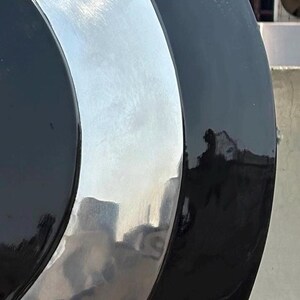Puede incluir: Primer plano de un objeto circular brillante con un anillo exterior negro, un anillo central plateado y un centro negro. La superficie reflectante refleja el entorno. El objeto parece ser de metal.