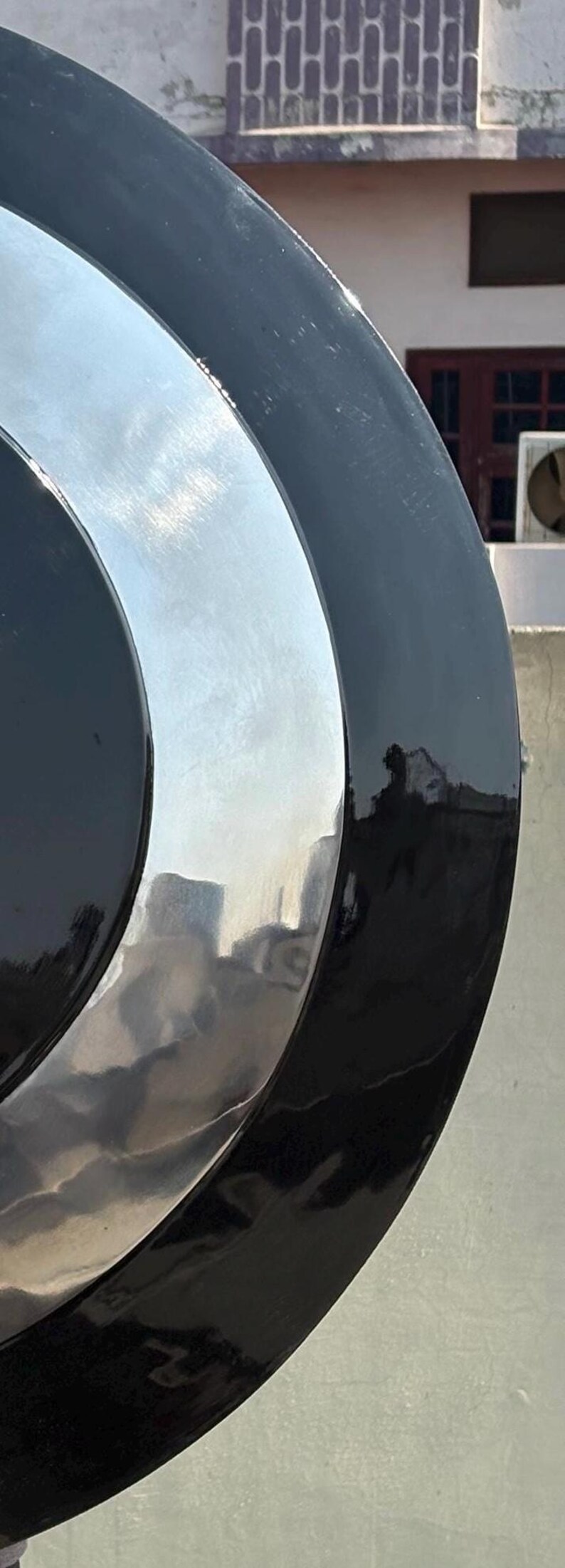 Puede incluir: Primer plano de un objeto circular brillante con un anillo exterior negro, un anillo central plateado y un centro negro. La superficie reflectante refleja el entorno. El objeto parece ser de metal.