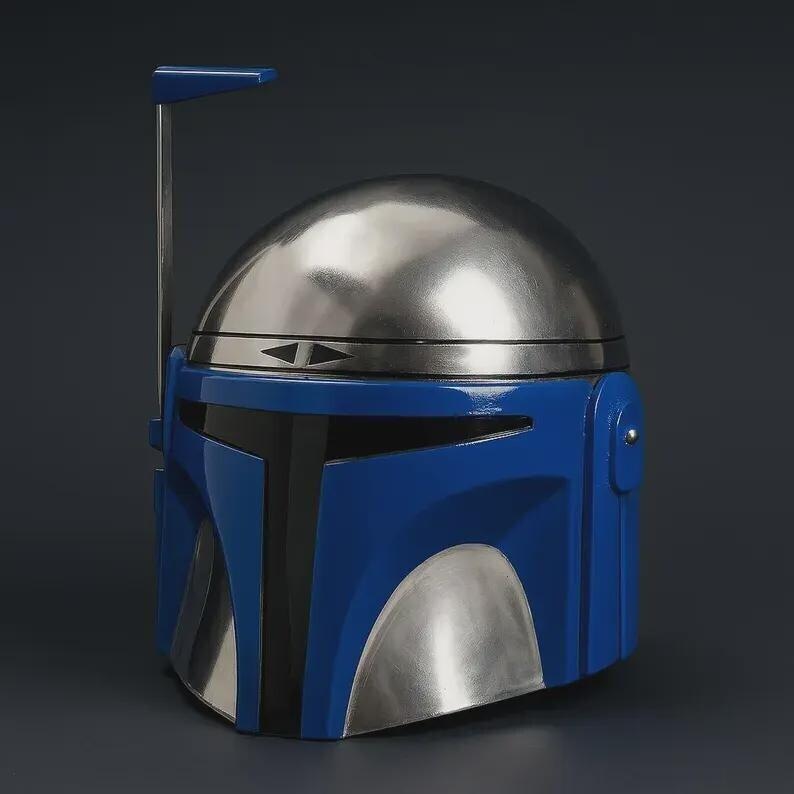 May include: A blue and silver Mandalorian helmet. The helmet features a rounded silver top, a blue faceplate, and a silver lower section. A vertical antenna extends from the top. The helmet is a replica from the Star Wars franchise.