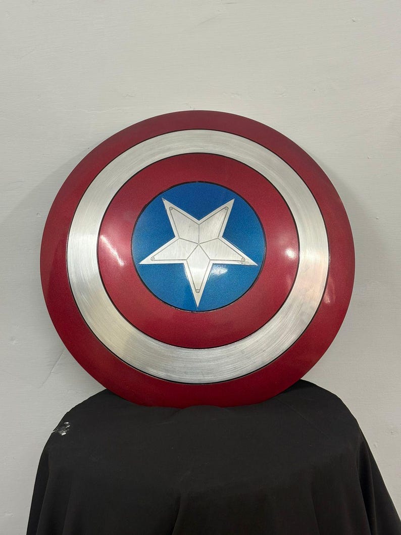 May include: A circular shield featuring a metallic red outer ring, a silver middle ring with a brushed texture, and a central blue circle containing a large, five-pointed silver star. The design is symmetrical with clean, defined color sections.