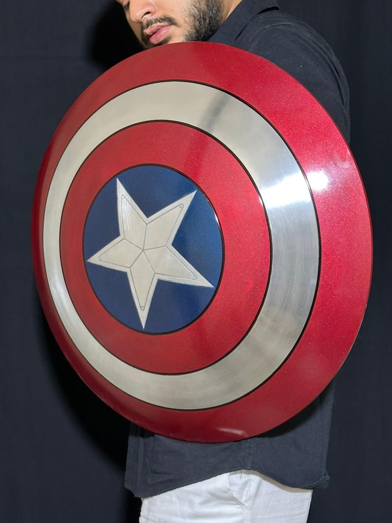 May include: A red, white, and blue Captain America shield. The shield is round with a silver outer ring, a red center, and a blue circle with a white star in the middle. The shield is a prop.