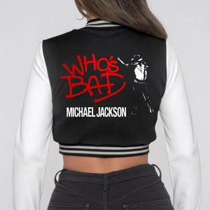 May include: Black and white varsity jacket with white sleeves. The back features the text "WHO'S BAD" in red, the name "MICHAEL JACKSON" in white, and a silhouette of Michael Jackson.
