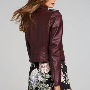 Pu&ograve; includere: Giacca in similpelle bordeaux in stile biker, con colletto a revers, zip asimmetrica e dettagli trapuntati sulle spalle. La giacca &egrave; abbinata a una gonna nera con stampa floreale.