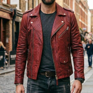 May include: A red leather biker jacket with a snakeskin pattern. The jacket has a notched collar, asymmetrical zipper closure, and multiple pockets. The model is wearing a gray t-shirt, dark wash jeans, and a brown leather belt. The jacket is a bold fashion statement.