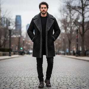 May include: A black shearling coat with a grey shearling collar and trim. The coat is worn over a black sweater and black trousers. The person is wearing brown leather boots. The background shows a city street with buildings and trees.