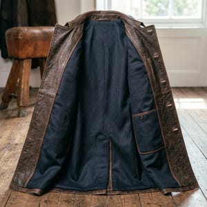 Pu&ograve; includere: Cappotto in pelle marrone aperto, che rivela una fodera interna blu scuro. Il cappotto &egrave; abbottonato e ha una tasca interna. Viene mostrato aperto, mostrando la sua costruzione. Poggia su un pavimento in legno.