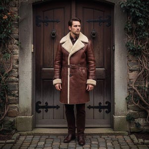 May include: A brown leather coat with cream shearling lining and trim. The coat has a belt at the waist and is worn with brown trousers and shoes. The background features a wooden door and stone wall.