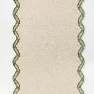 May include: A rectangular, off-white placemat with a scalloped edge. The edge is trimmed with a woven, olive green border. The placemat has a textured appearance and is set against a white background.