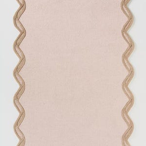 May include: A rectangular, blush-colored rug with a scalloped edge. The border is a light tan color, creating a contrasting frame. The rug has a soft, textured appearance, suitable for home decor.