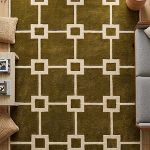 May include: An olive green area rug with a geometric pattern of white rectangles and lines. The rug is rectangular and has a soft, plush texture. The design is symmetrical and modern, suitable for a living room or bedroom.