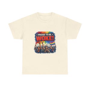 May include: Cream-colored t-shirt featuring a colorful graphic with the text "PROUD TO BE WOKE!" above a crowd of people holding flags and raising their fists. The graphic includes a rainbow and stars.