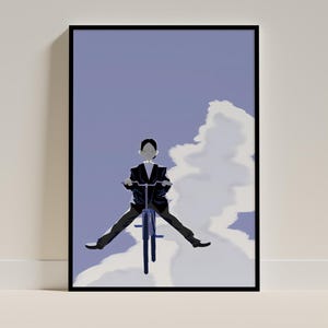 May include: A framed art print featuring a person riding a bicycle in the sky. The person is wearing a black suit and is positioned against a light blue sky with a large cloud. The artwork has a minimalist style.