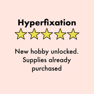 Op de afbeelding: Lichtroze achtergrond met het woord "Hyperfixation" in zwart boven vier gele sterren. Onder de sterren staat de tekst "Nieuwe hobby ontgrendeld. Benodigdheden al gekocht."
