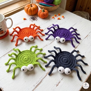 May include: Four crocheted spider coasters in orange, purple, lime green, and black. Each spider features a circular body, eight spindly legs, and two white round eyes with black pupils. The coasters are arranged on a white wooden surface.