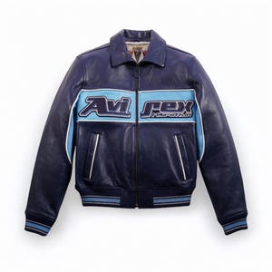 K&ouml;nnte beinhalten: Dunkelblaue Lederjacke mit hellblauem Streifen auf der Brust, mit dem Text "Avi Rex". Die Jacke hat einen Kragen, einen Rei&szlig;verschluss und gerippte B&uuml;ndchen und Saum. Wei&szlig;e Zierleisten akzentuieren den hellblauen Streifen und die Taschen.