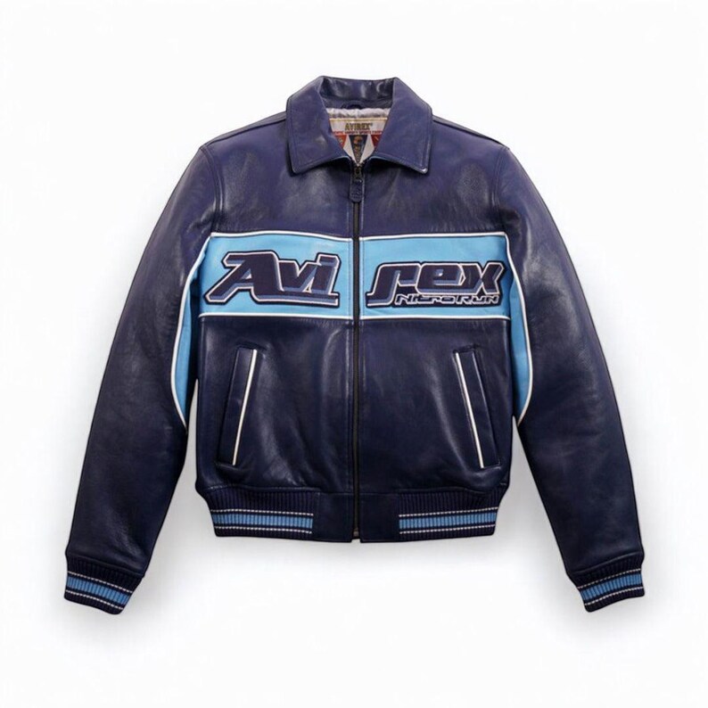 K&ouml;nnte beinhalten: Dunkelblaue Lederjacke mit hellblauem Streifen auf der Brust, mit dem Text "Avi Rex". Die Jacke hat einen Kragen, einen Rei&szlig;verschluss und gerippte B&uuml;ndchen und Saum. Wei&szlig;e Zierleisten akzentuieren den hellblauen Streifen und die Taschen.
