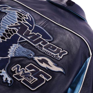 K&ouml;nnte beinhalten: Nahaufnahme einer marineblauen Lederjacke mit gestickten Aufn&auml;hern. Die Aufn&auml;her zeigen ein Adlerdesign und den Text "Avirex Nitro Run" und "M35" in Wei&szlig; und Blau. Wei&szlig;e Paspeln akzentuieren die N&auml;hte der Jacke.