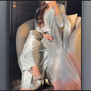 May include: A light blue formal outfit, including a long-sleeved top, wide-leg pants, and a sheer scarf. The outfit is embellished with floral embroidery and sparkling accents. The matching shoes and clutch are also adorned with shimmering details.