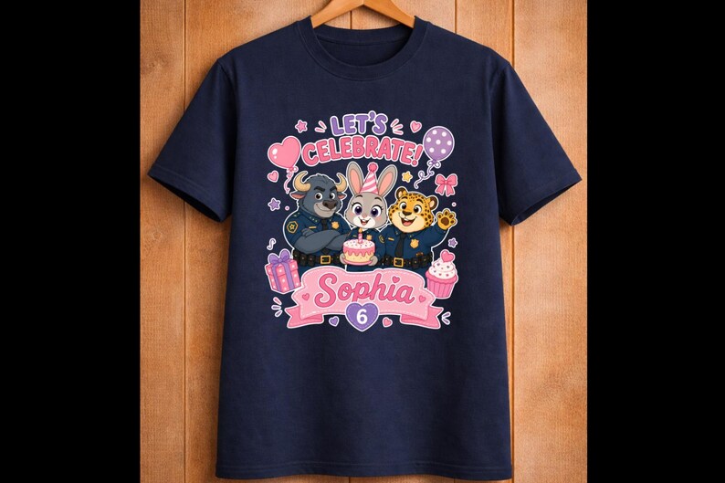 May include: Navy blue t-shirt featuring cartoon characters from Zootopia. The design includes the text "Let's Celebrate!" and "Sophia 6" with a cake, balloons, and gifts. The shirt is hanging on a wooden hanger.
