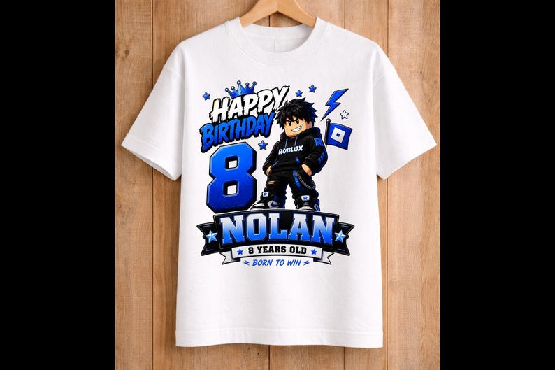 May include: White t-shirt with a blue and black graphic design. The design includes the words "Happy Birthday" above a large blue number "8", the name "Nolan", and the phrase "8 Years Old Born to Win". A cartoon character is also featured.