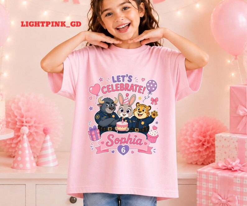 May include: A light pink t-shirt featuring a colorful graphic of cartoon characters, a cake, and the text "LET'S CELEBRATE!" and "Sophia 6". The shirt is short-sleeved and suitable for a birthday celebration.