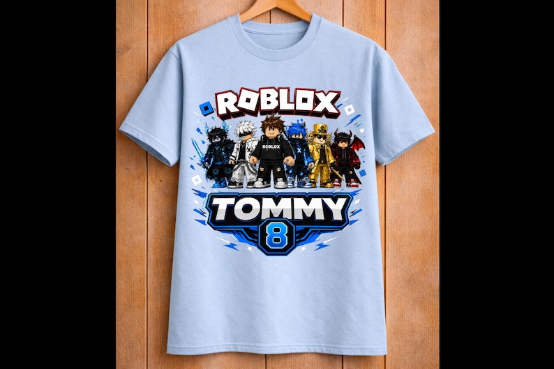 May include: Light blue Roblox-themed t-shirt featuring a group of cartoon characters. The shirt has the word "ROBLOX" in red and white, with the name "TOMMY" and the number "8" in blue and white.