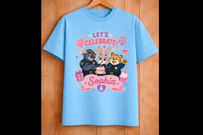 May include: Light blue t-shirt featuring a birthday design with cartoon characters. The shirt has the text "LET'S CELEBRATE!" and the name "Sophia" with the number "6". Includes images of a cake, balloons, and cupcakes.