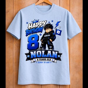 May include: Light blue t-shirt with a graphic design for an 8th birthday. The design includes the words "Happy Birthday," the number "8" in blue, and the name "Nolan." A cartoon character is also featured.