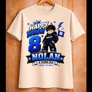 May include: A beige t-shirt with a blue and black graphic design. The design includes the words "HAPPY BIRTHDAY" above a large blue number "8", the name "NOLAN", and the phrase "8 YEARS OLD". A cartoon character is also featured.