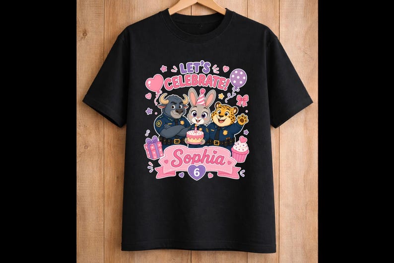 May include: Black t-shirt featuring a colorful graphic with the text "Let's Celebrate!" and the name "Sophia" with the number "6". The design includes cartoon characters, balloons, and a cupcake.