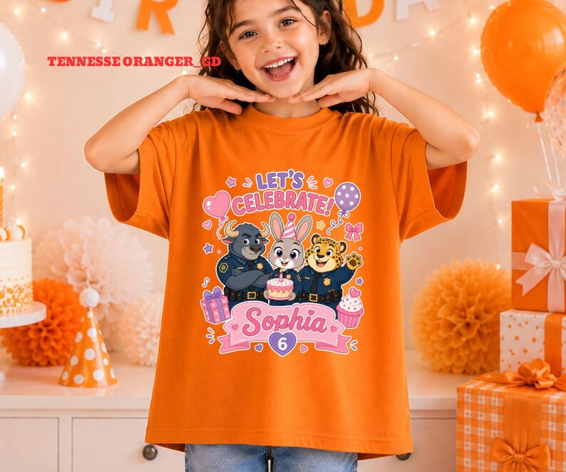 May include: Orange t-shirt featuring a colorful graphic with the text "LET'S CELEBRATE!" and the name "Sophia" with the number "6". The graphic includes cartoon characters, balloons, and a cupcake.