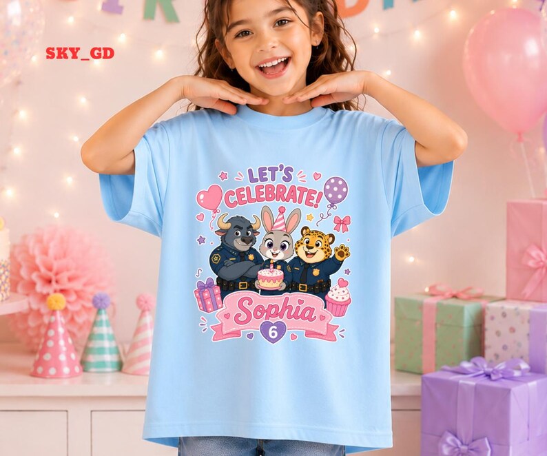 May include: A light blue t-shirt featuring a colorful graphic of cartoon characters from Zootopia, with the text "LET'S CELEBRATE" and the name "Sophia" with the number "6". The design includes a cake, balloons, and gift boxes.