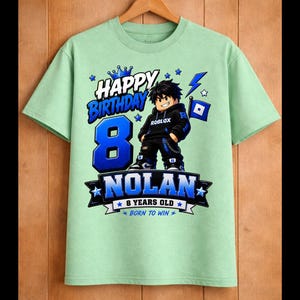 May include: A light green t-shirt with a birthday theme. The shirt features the text "HAPPY BIRTHDAY" and the number "8" in blue. A cartoon character is in the center, with the name "NOLAN" below. The shirt also says "8 YEARS OLD" and "BORN TO WIN".