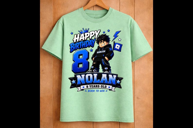 May include: A light green t-shirt with a birthday theme. The shirt features the text "HAPPY BIRTHDAY" and the number "8" in blue. A cartoon character is in the center, with the name "NOLAN" below. The shirt also says "8 YEARS OLD" and "BORN TO WIN".