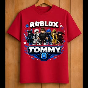 May include: Red t-shirt featuring a Roblox graphic with multiple characters. The shirt has the text "ROBLOX" above a graphic that says "TOMMY 8". The design includes blue and white accents.