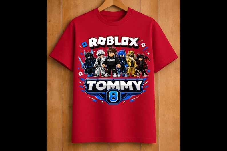 May include: Red t-shirt featuring a Roblox graphic with multiple characters. The shirt has the text "ROBLOX" above a graphic that says "TOMMY 8". The design includes blue and white accents.