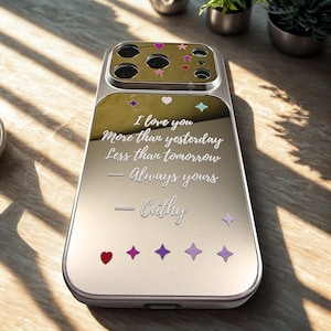 May include: Silver phone case with a mirrored finish, adorned with colorful star and heart-shaped embellishments. The case features the engraved text "I love you More than yesterday Less than tomorrow - Always yours - Cathy."