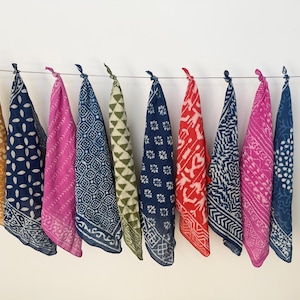 May include: Ten square bandanas hanging from a horizontal wire, each featuring distinct block-printed patterns in colours including mustard yellow, navy blue, magenta, olive green, and red, with white geometric, floral, and abstract motifs.
