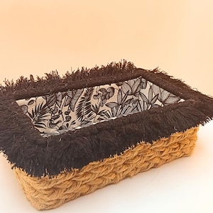 Può includere: Cesto rettangolare intrecciato con esterno marrone naturale e finiture con frange nere. L'interno presenta una fodera con stampa botanica in bianco e nero. Il cesto è progettato per la conservazione e la decorazione.