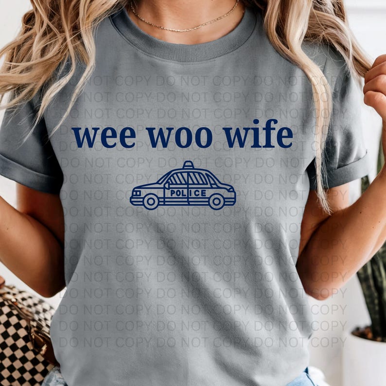 May include: Gray t-shirt with the text "wee woo wife" in navy blue above a navy blue police car graphic. The word "POLICE" is printed on the side of the car.