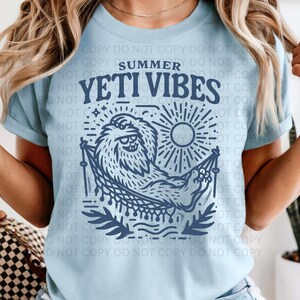 Może przedstawiać: Jasnoniebieska koszulka z napisem "Summer Yeti Vibes" i niebieską grafiką yeti relaksującego się w hamaku pod słońcem. Projekt jest w odcieniach niebieskiego.