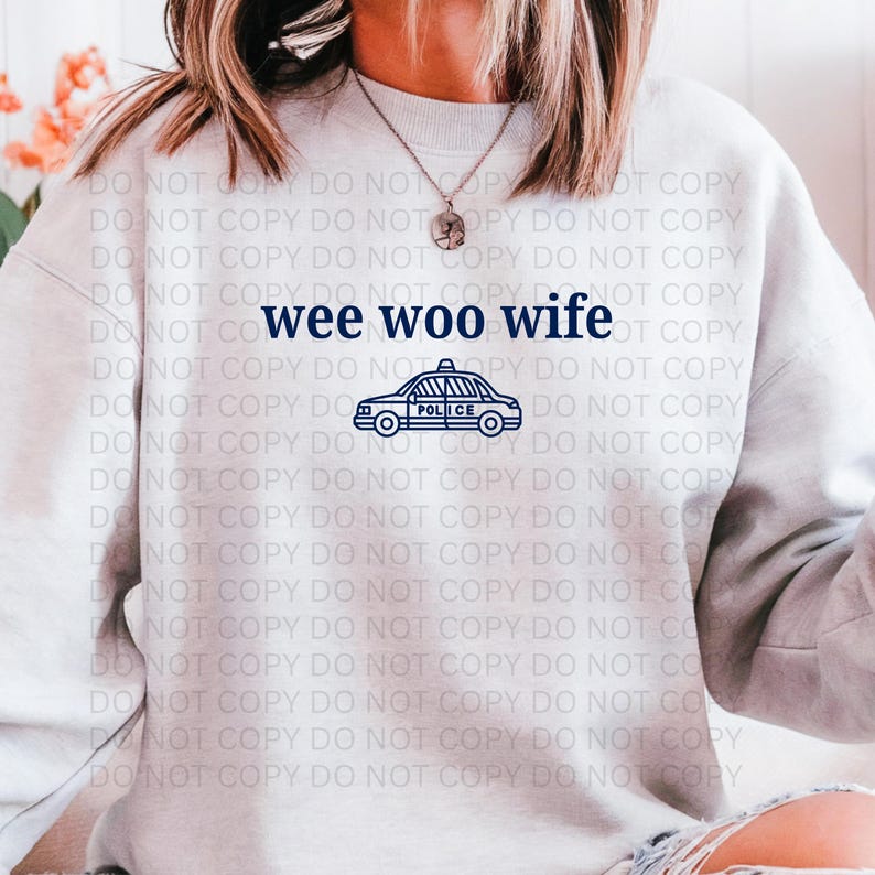 May include: A light gray sweatshirt with the text "wee woo wife" in navy blue, along with a navy blue police car graphic. The sweatshirt is a casual style.
