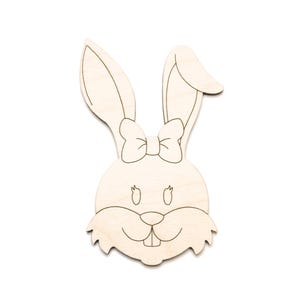 May include: A wooden bunny head cutout with a bow, ears, and a smiling face. The bunny is made of light-colored wood. Text at the bottom reads: Please check exact measurements before ordering. See listing images & listing info.